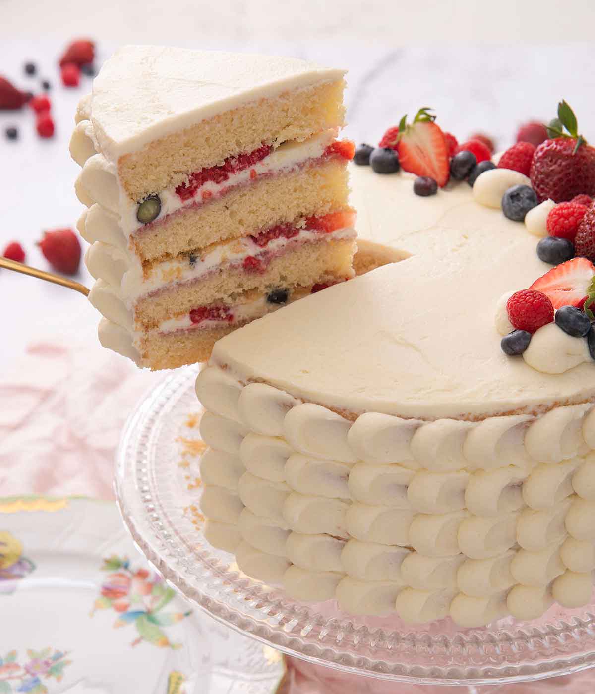 A slice of Chantilly cake being lifted from the cake on a cake stand.
