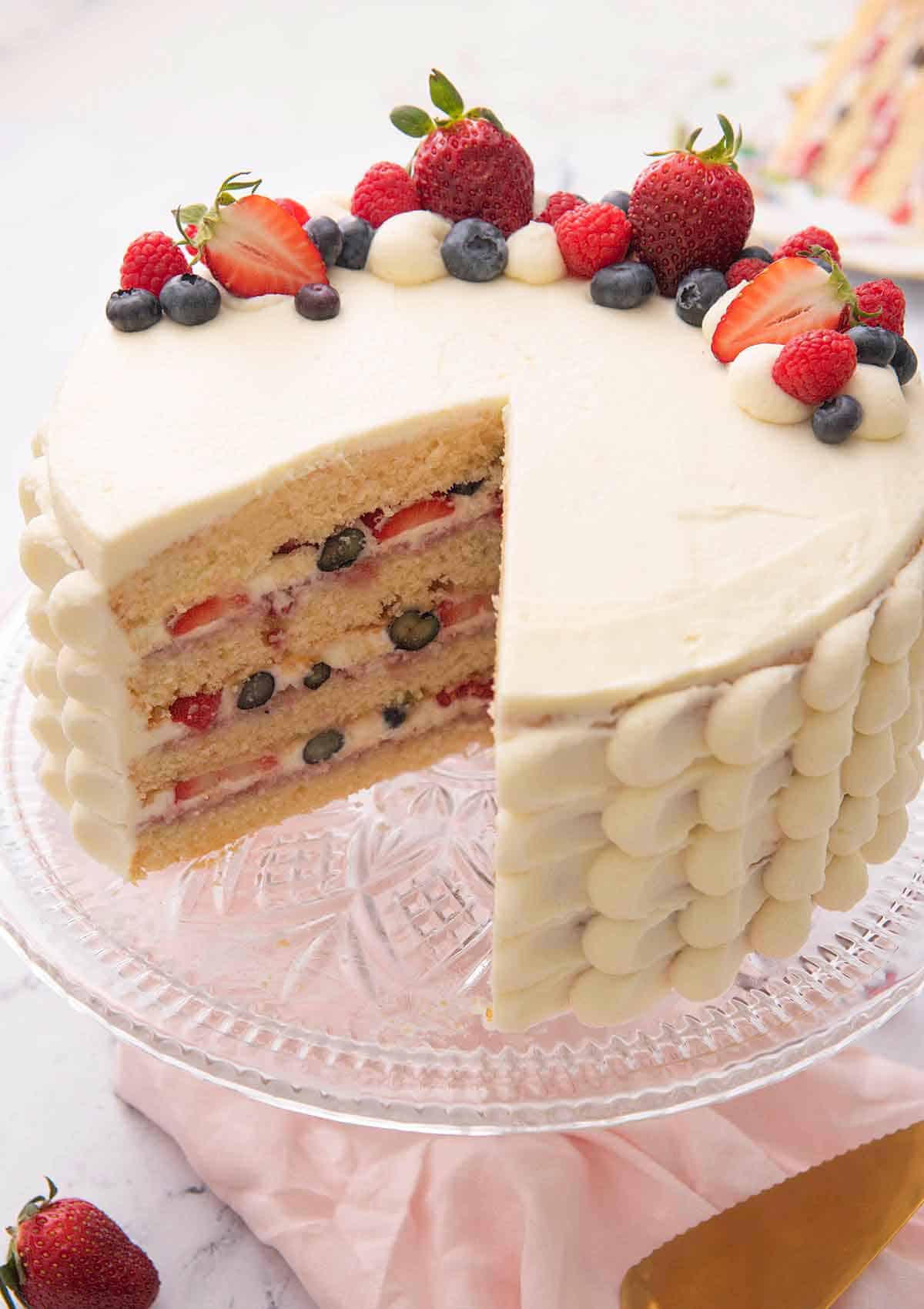 A Chantilly cake with a slice cut out showing the four tiers with berries in between.