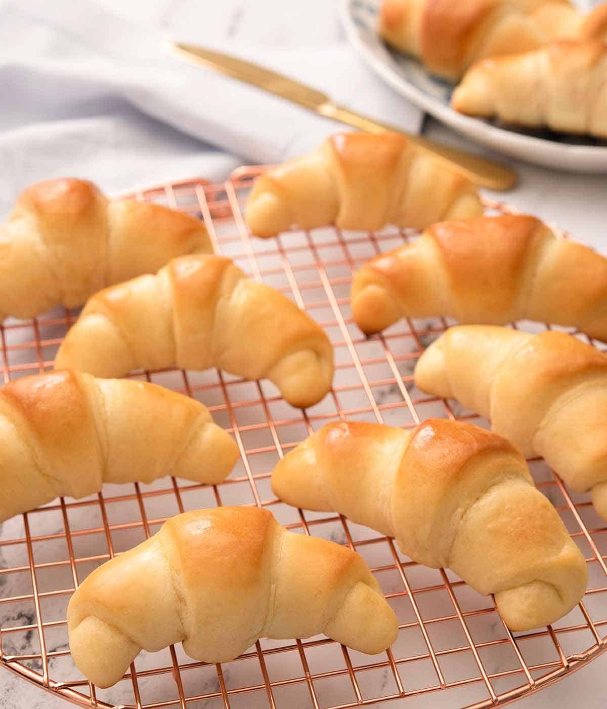 Eight crescent rolls on a rose gold circular cooling rack.