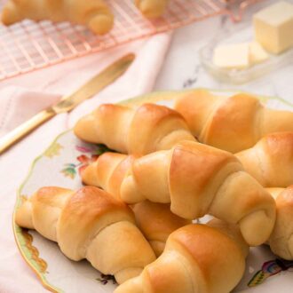 Pinterest graphic of rolls piled on to a plate beside a folded pink linen napkin and a cooling rack with rolls cooling on top.