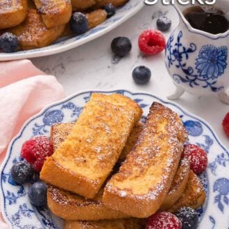 Pinterest graphic of a plate with a stack of French toast sticks and fresh fruit with a serving platter with more in the background.