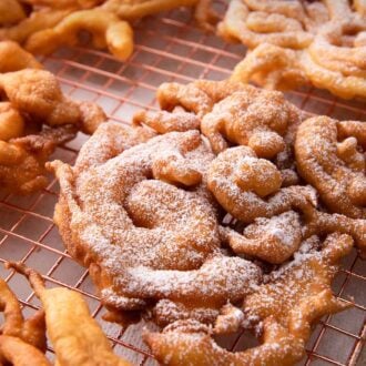 Pinterest graphic of a cooling rack with multiple funnel cakes with two with powdered sugar.
