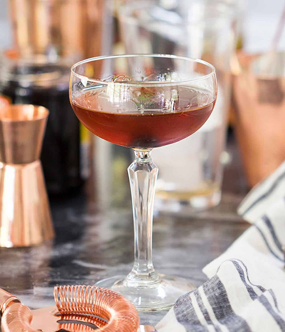 A Manhattan in a cocktail glass behind a linen napkin and strainer.