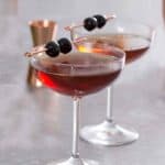 Two manhattan cocktails with two maraschino cherries on a pick on top of each drink.