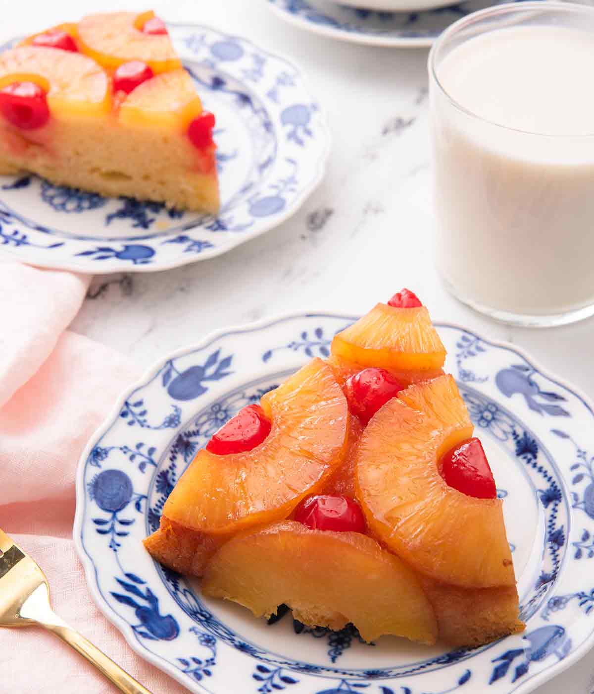 Two slices of pineapple upside down cake on blue and white plates with one in the foreground.