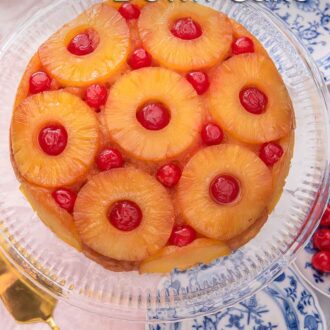 Pinterest graphic of an overhead view of a pineapple upside down cake on a clear cake stand.