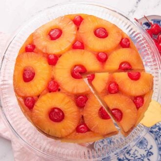 Overhead view of a pineapple upside down cake on a cake stand with a slice being lifted up.