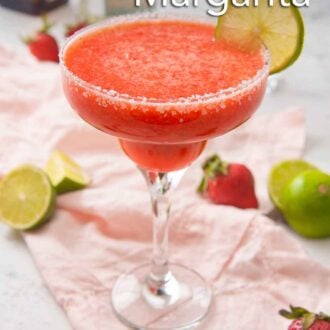 Pinterest graphic of a strawberry margarita in a cocktail glass with salt on the rim and a slice of lime as garnish on top of a pink linen napkin. Halved limes and strawberries are around it.