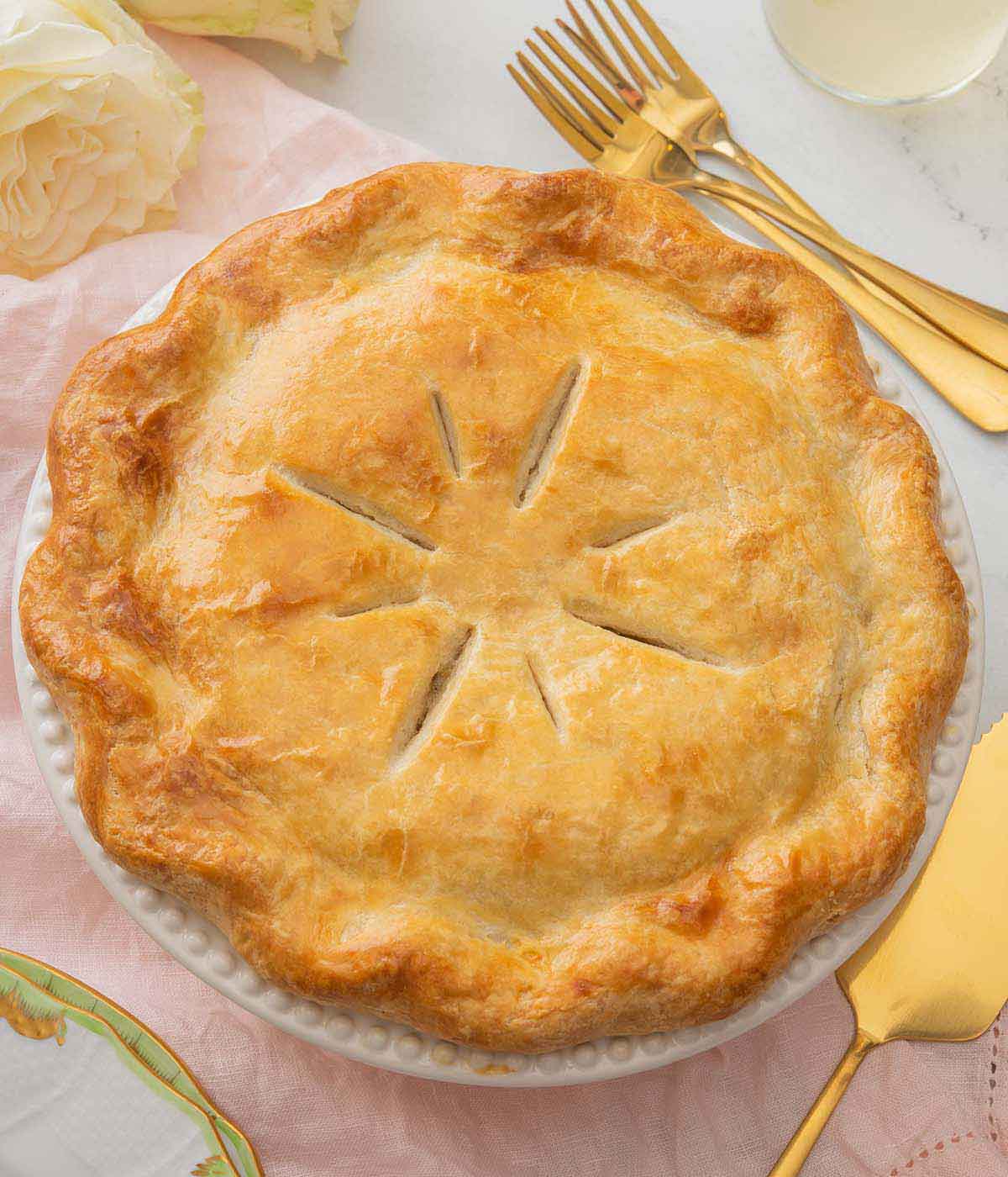 Overhead view of a turkey pot pie in a white pie dish over top of a pink linen napkin.