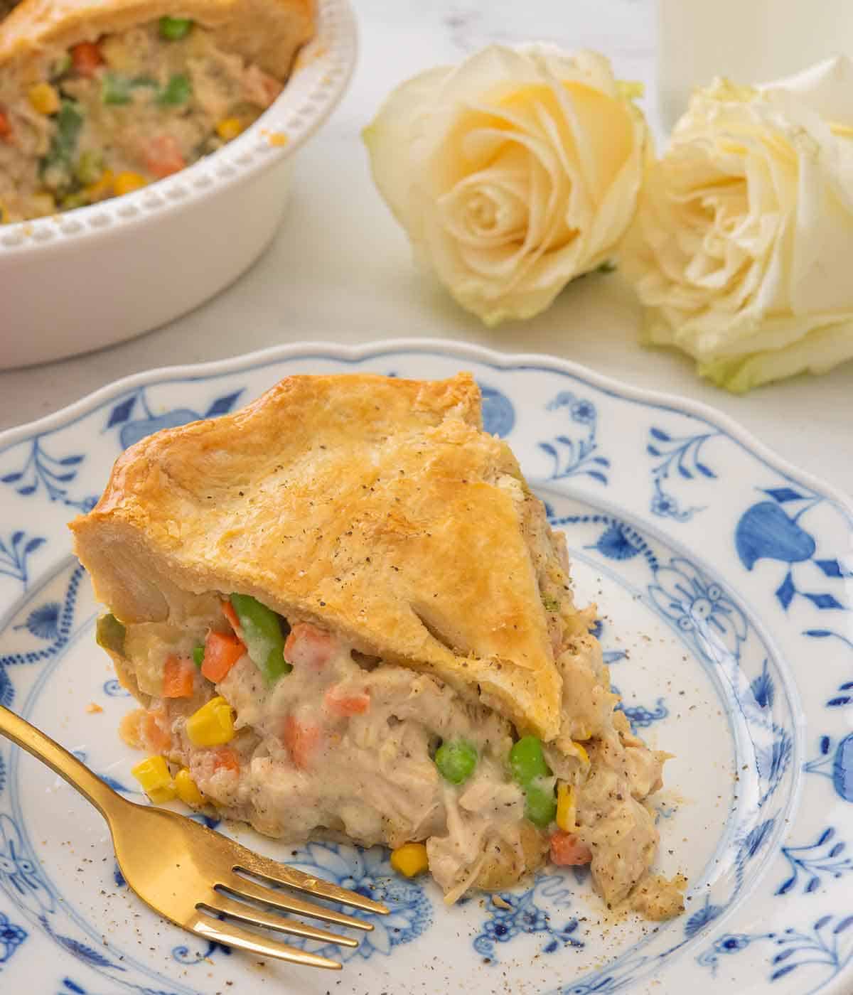 Close up of a slice of turkey pot pie on a white and blue plate with two white roses in the background.