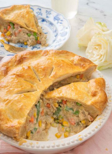 A turkey pot pie, cut opened with a slice removed and placed on a plate behind it.