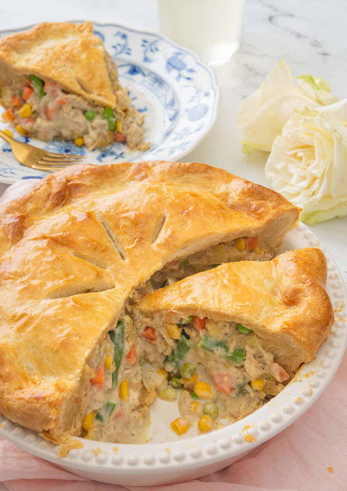 A turkey pot pie, cut opened with a slice removed and placed on a plate behind it.