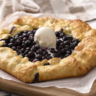 A blueberry galette topped with a scoop of vanilla ice cream on a cutting board.