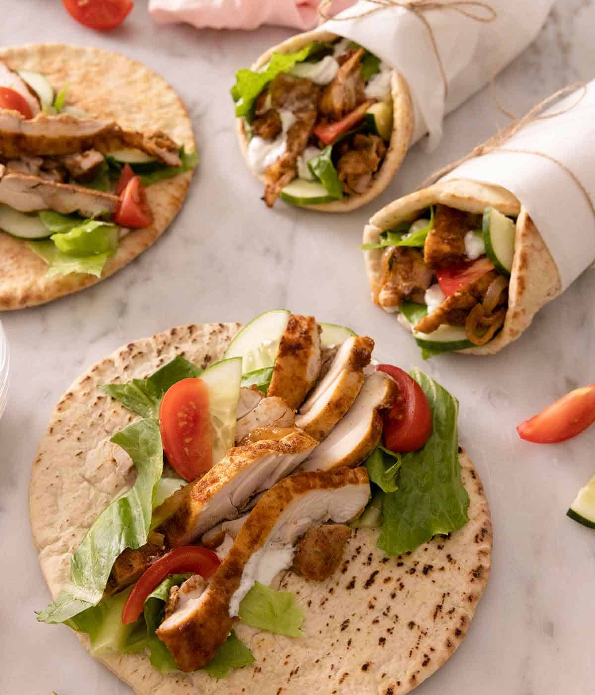 Two parchment wrapped chicken shawarma with two opened pitas in front.