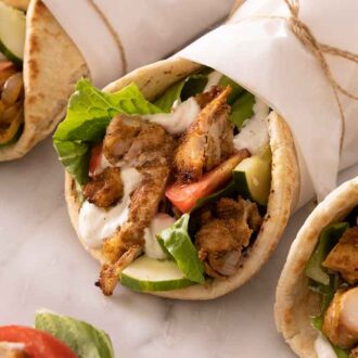 Three chicken shawarma with one in focus, all wrapped in parchment paper.