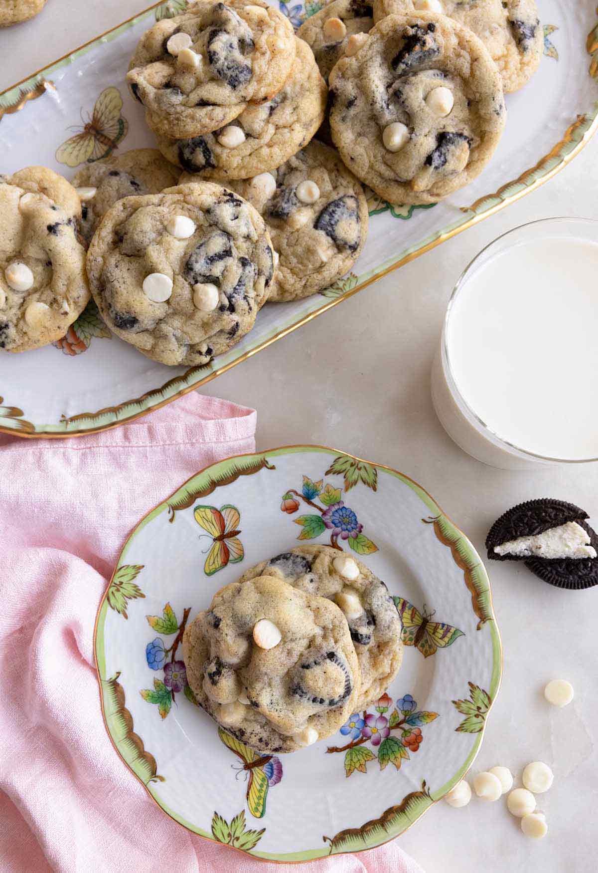 Overhead view of a serving platter of cookies and cream cookies with a small plate of them off to the side with a glass of milk.