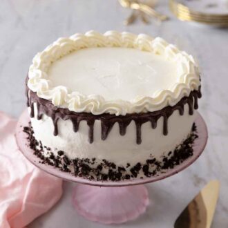 Pinterest graphic of an ice cream cake on a pink cake stand with a pink linen on the counter with a cake spatula.