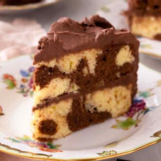 Close up of a slice of marble cake with chocolate frosting on a plate with a pink linen napkin and fork beside it.