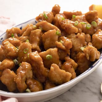 A platter of orange chicken with green onions.