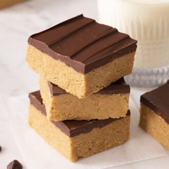 A stack of three peanut butter bars with one beside it. Glass of milk in the back.