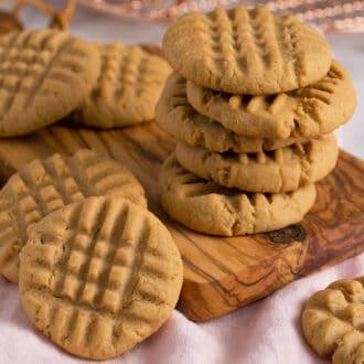 A group of peanut butter cookies stacked on a small wooden board.