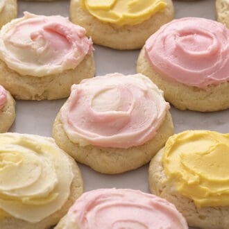 A group of sour cream cookies topped with pink and yellow buttercream on a marble surface.