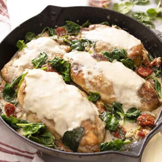An iron skillet with creamy tuscan chicken on a marble surface.