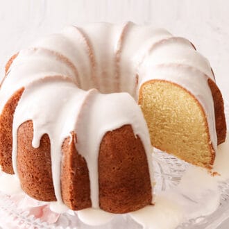 A vanilla bundt cake with icing on a glass cake stand.