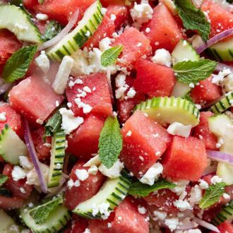 Close up of a watermelon salad with cubed watermelon, cucumbers, onions, feta, and mint.