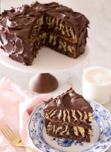 A slice of zebra cake on a plate in front of the rest of the cake behind it on a cake stand.