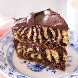 Close up of a slice of zebra cake with chocolate frosting on a blue and white plate.
