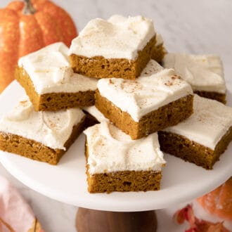 A stack of pumpkin bars with cream cheese frosting on a cake stand.