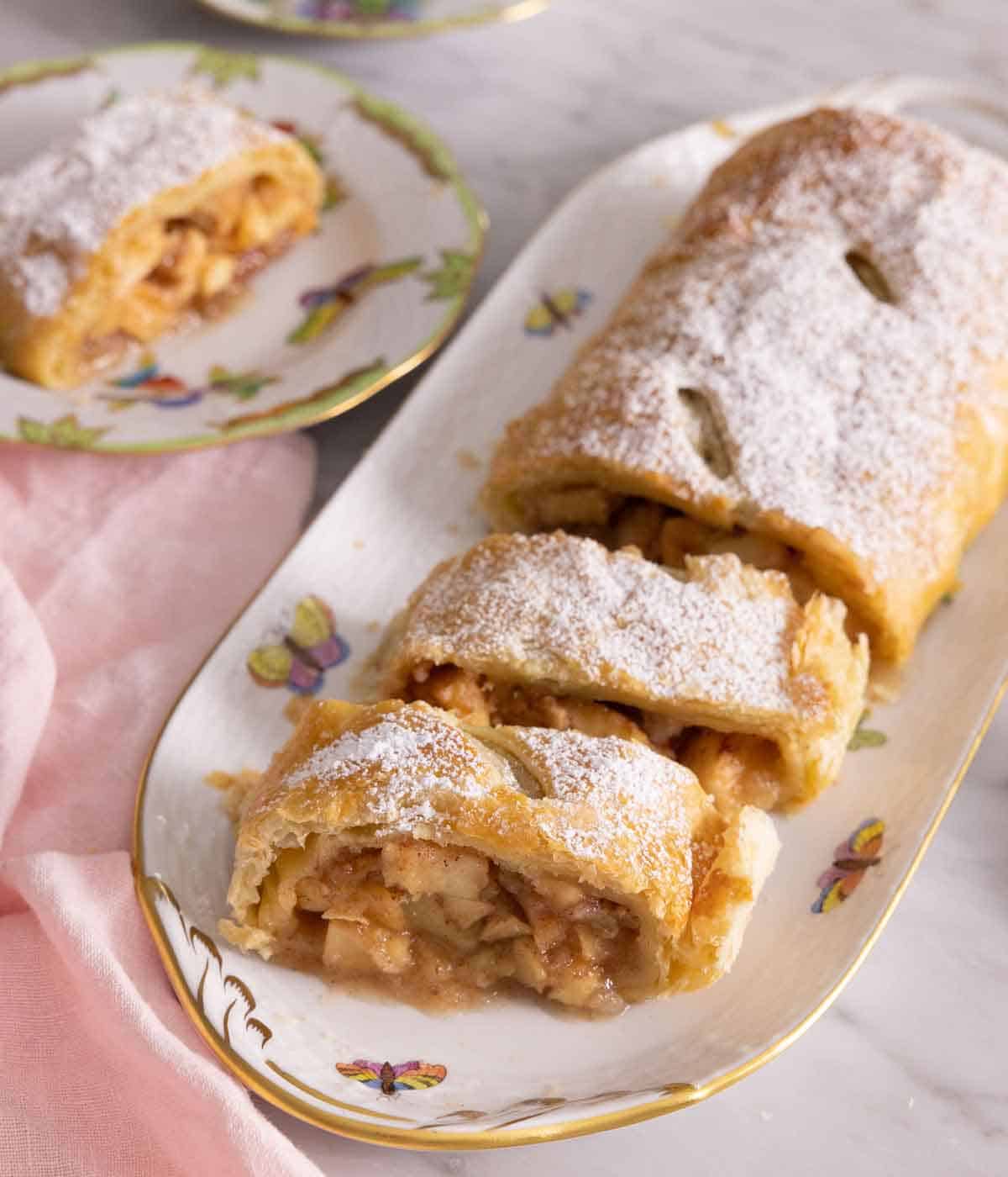 A serving platter of apple strudel with slices cut.