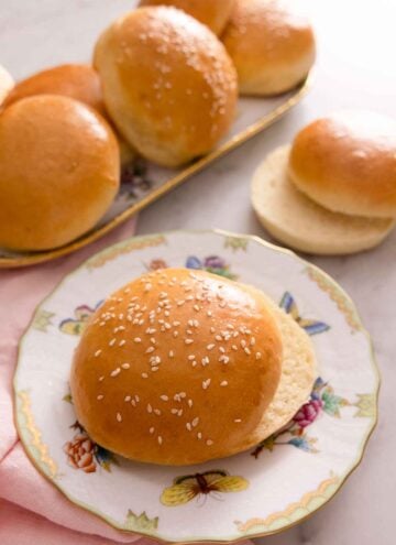A plate with a brioche bun, sliced in half with more in the background on a platter.