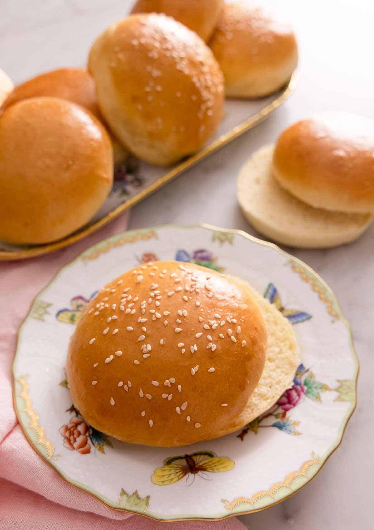 A plate with a brioche bun, sliced in half with more in the background on a platter.