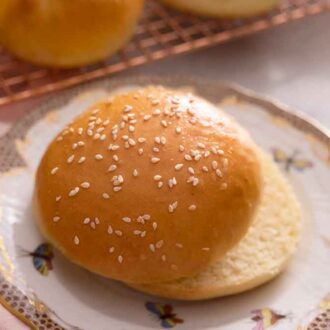 A brioche bun with sesame seeds on top, cut in half on a plate.