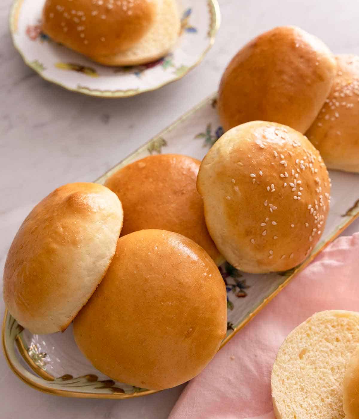 A serving platter of brioche buns with a couple of them topped with sesame seeds.