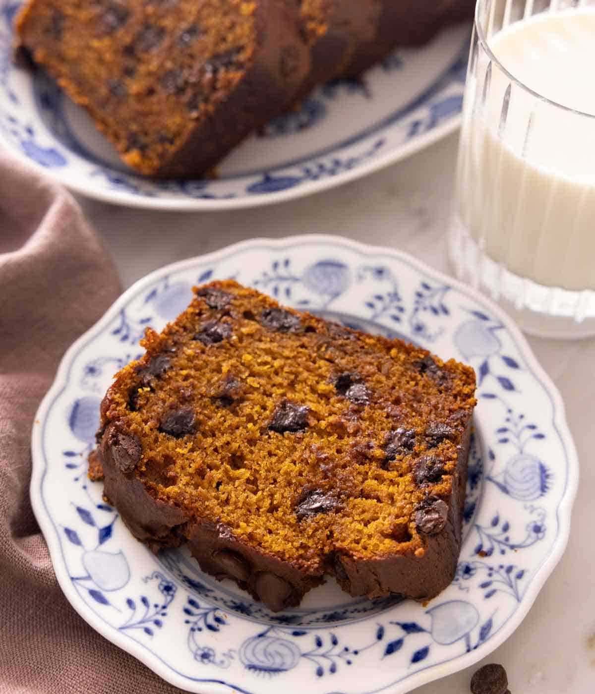 A slice of chocolate chip pumpkin bread on a plate with a cup of milk in the background.
