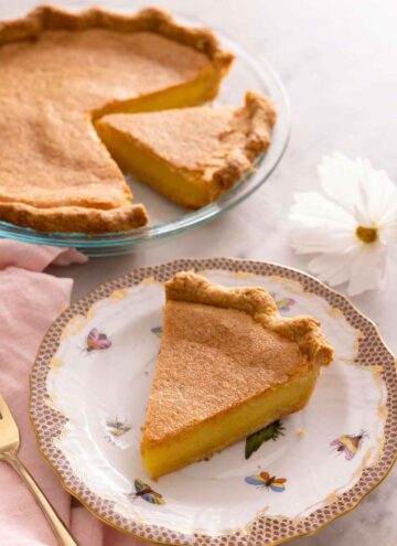 A slice of chess pie on a plate in front of the rest of the pie in the background.