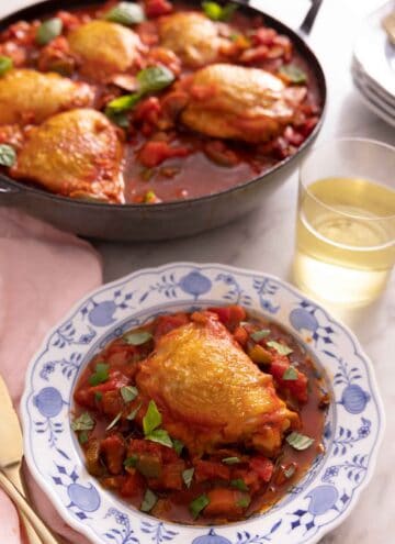 A plate with a serving of chicken cacciatore in front of a pan with more chicken.