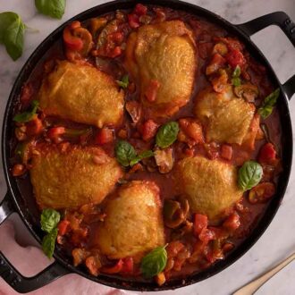Overhead view of chicken cacciatore in a pan with a linen napkin and spoon beside it.