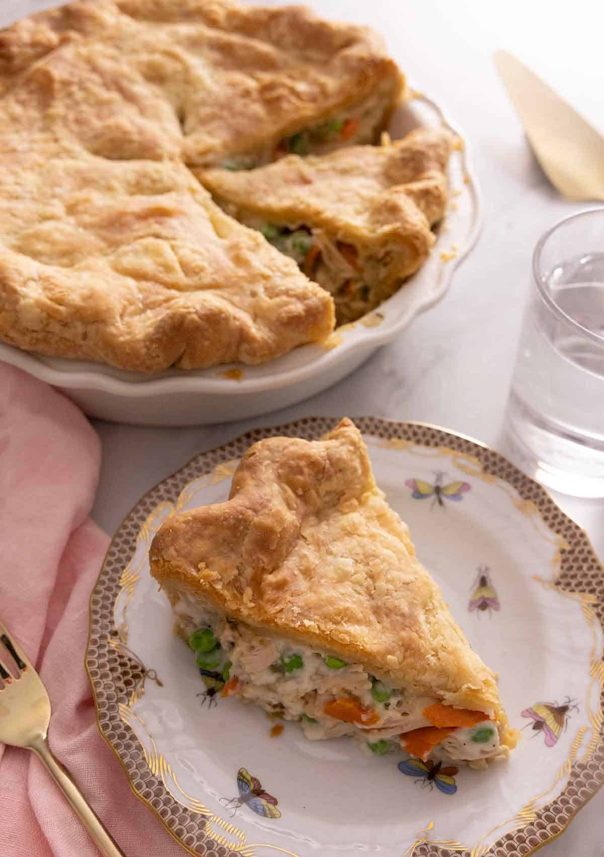 A slice of chicken pot pie on a plate in front of the rest of the pie.