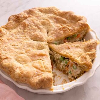 A chicken pot pie in the baking dish with some slices cut, beside a pink linen napkin.