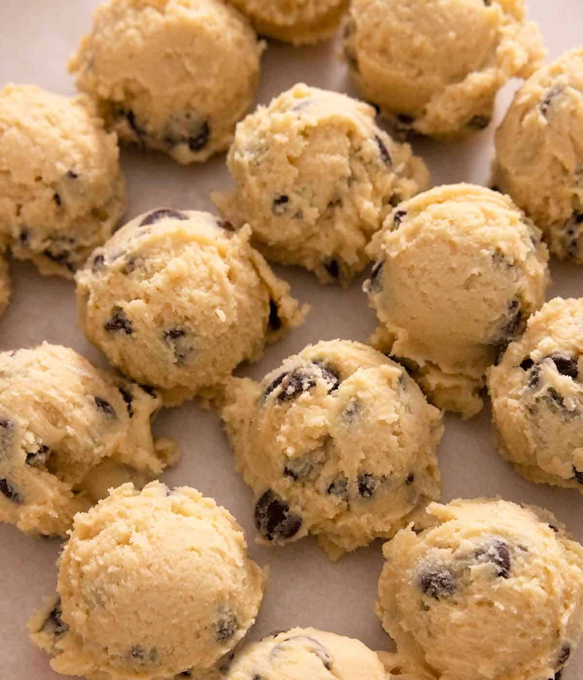 Multiple scoops of raw cookie dough on a lined sheet pan.