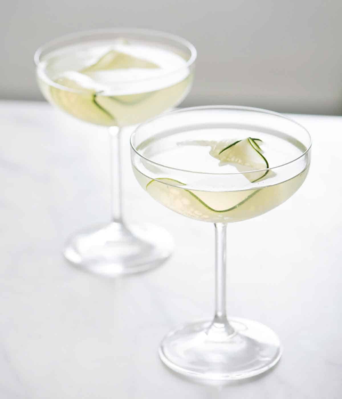 Two glasses of cucumber martini with sliced cucumber as garnish.