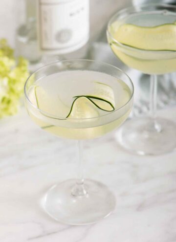 Two glasses of cucumber martini with one in front of the other. Both has a thin slice of cucumber as garnish.