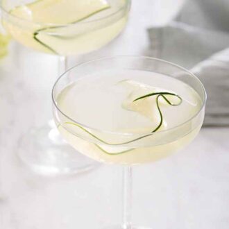 A glass of cucumber martini with a linen napkin in the background and a second martini out of focus.