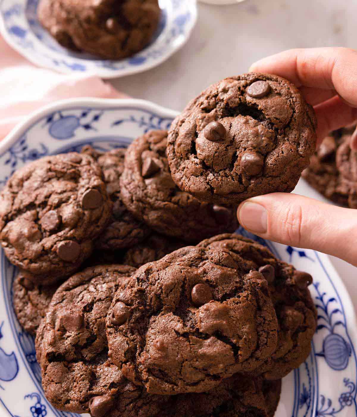 A hand lifting up a double chocolate chip from a platter of cookies.