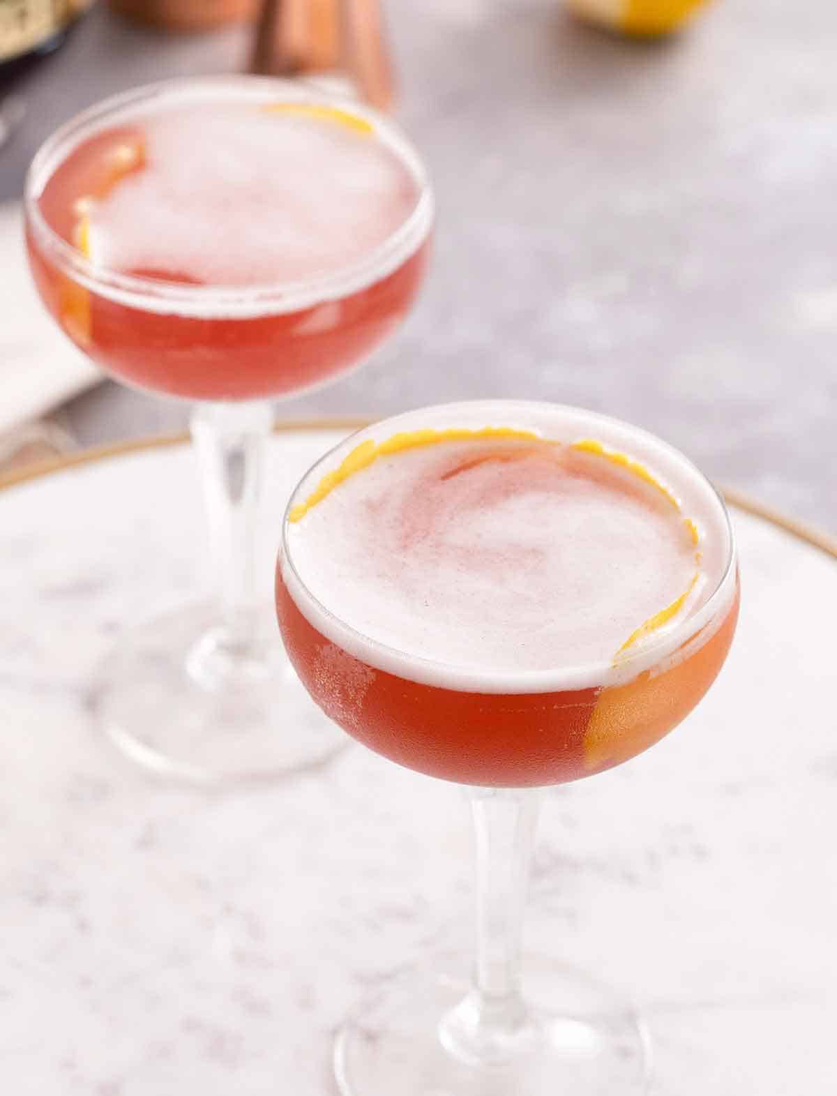 Angled view showing the top of two cocktail glasses containing French martinis with a lemon peel in each as a garnish.
