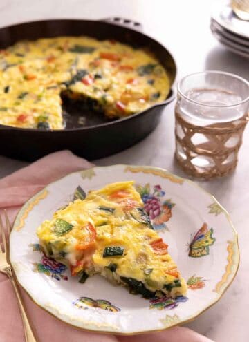 A plate with a slice of frittata with the skillet with the rest of the frittata in the background.